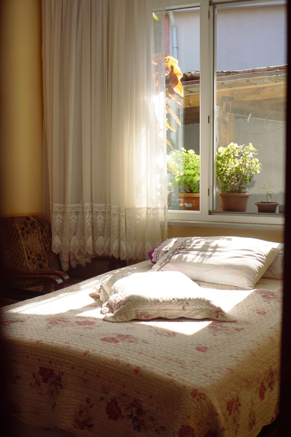 Chambre chaleureuse au petit matin, lit fait et rideaux de dentelle traversés par le soleil
