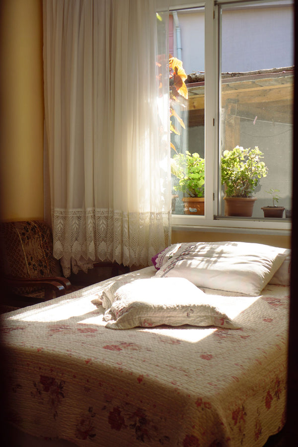 Chambre chaleureuse au petit matin, lit fait et rideaux de dentelle traversés par le soleil