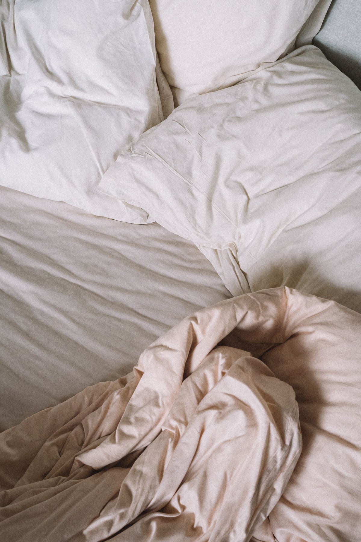 Lit défait aux draps clairs dans une chambre le matin