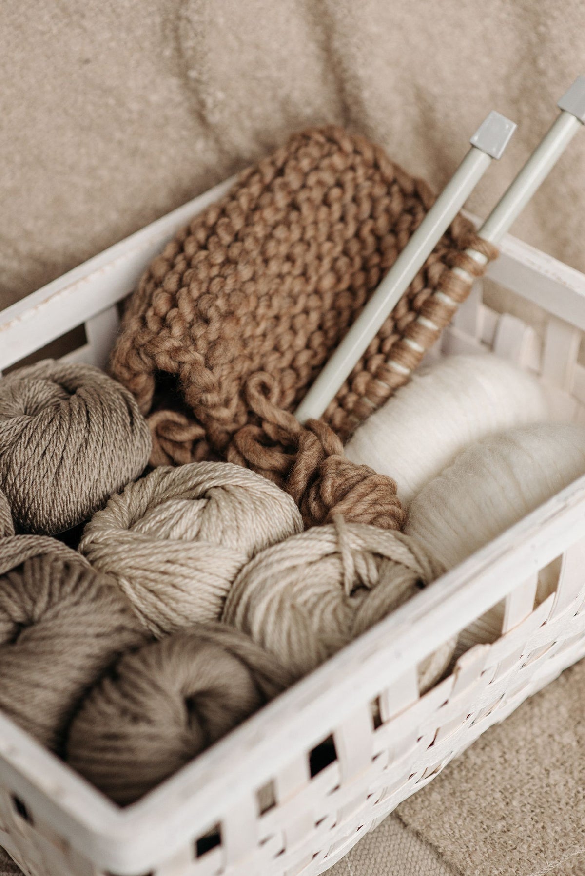 Panier en osier rempli de pelotes de laine beige et d'un tricot en cours avec aiguilles