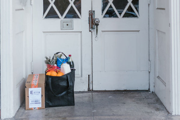 Sac de courses et carton posés devant une porte d'entrée